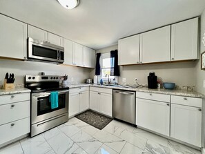 A modern kitchen with white cabinets, stainless steel appliances, a microwave, oven, and dishwasher.