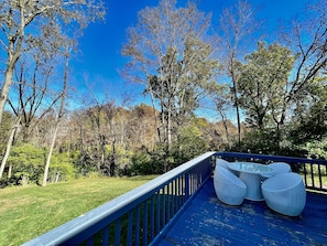 A blue deck with white wicker furniture, surrounded by trees and a clear sky.
