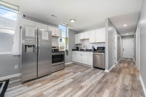 A modern kitchen with stainless steel appliances, white cabinetry, and a herringbone wood floor. - 101 Crawford Street unit B · Funky Firehouse Renovated into Modern 2 BDR/1 Bath (Middletown)