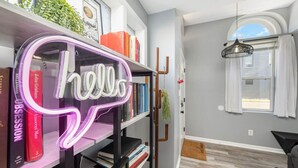Une pièce avec une bibliothèque, un néon affichant le mot « bonjour », une fenêtre avec des rideaux et un luminaire suspendu.