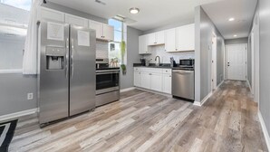 Une cuisine moderne dotée d’appareils électroménagers en acier inoxydable, de meubles blancs et d’un parquet en bois disposé en motif chevrons.