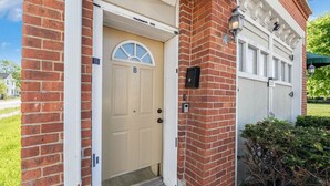Un bâtiment de deux étages en briques, avec une porte d’entrée beige, un petit porche et une porte de garage.