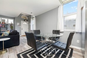 A modern living room with a glass-top dining table, black leather chairs, a dark sofa, and a patterned rug. - 101 Crawford Street unit B · Funky Firehouse Renovated into Modern 2 BDR/1 Bath (Middletown)