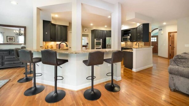 Una cocina moderna con una isla central, taburetes de bar y un área de comedor con un sofá de color oscuro.