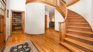 Un interior espacioso con una escalera de madera curvada, un pasillo que conduce a una biblioteca y un área de estar.