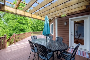 A covered deck with a table and chairs, a wooden railing, and a door leading to a room.