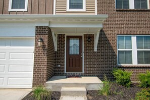 A two-story residential building with a front garage, a brown front door, and a small porch.