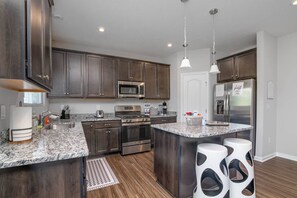 A modern kitchen with dark wood cabinets, stainless steel appliances, granite countertops, and a central island with stools.