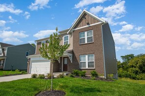 A two-story residential building with a garage, a small tree in the front yard, and a clear blue sky.