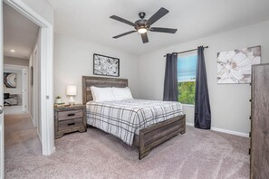 A bedroom with a bed, nightstands, a ceiling fan, and artwork on the walls.