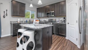 Una cocina moderna con armarios de madera oscura, una isla central con taburetes de bar, electrodomésticos de acero inoxidable y un ventanal que proporciona luz natural.