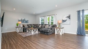 Un salón amplio con un sofá modular, dos mesitas auxiliares y un gran ventanal con cortinas.