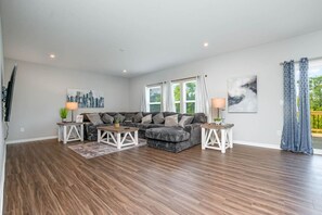 A spacious living room with a sectional sofa, two side tables, and a large window with curtains.