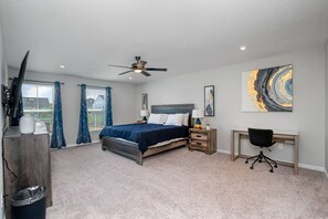 A bedroom with a bed, a desk, a chair, a ceiling fan, and artwork on the wall.
