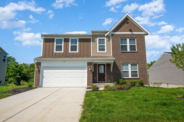 A two-story residential building with a garage, brick facade, and a well-maintained lawn.