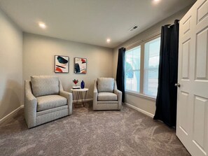A room with two armchairs, a small table with decorative items, and a window with blinds.
