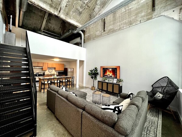 A modern living room with a sectional sofa, a fireplace, and a kitchen in the background.