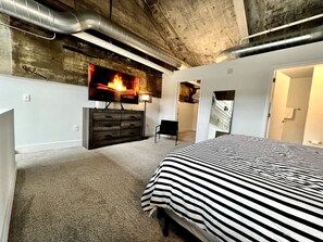 A bedroom with a bed, a dresser, a chair, and a fireplace.
