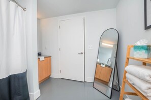 A small, clean room with a white door, a wooden cabinet, a mirror, and a shelf with towels.