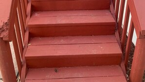 Een paar rode houten trappen met een metalen leuning, die leiden naar de ingang van een gebouw.