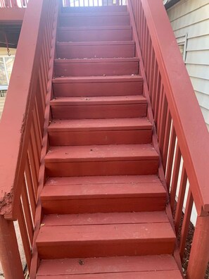 Eine Treppe aus rotem Holz mit Metallgeländer, die zu einem Hauseingang führt.