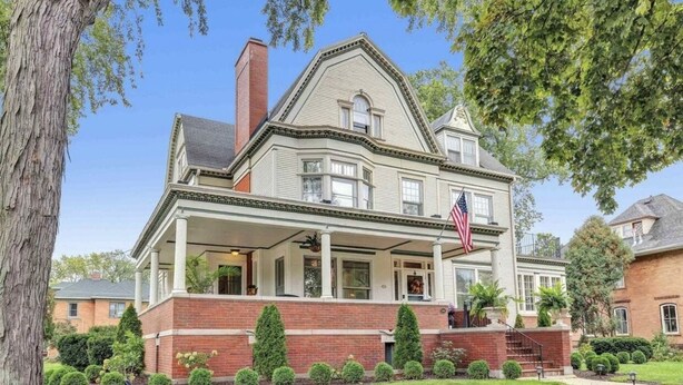 A two-story house with a wrap-around porch, a brick foundation, and a large American flag. - Tower Suite in Historic Mansion B&B, 9 min from Lambeau Field (Green Bay)
