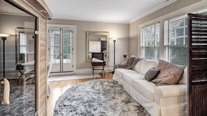 A living room with a beige sofa, a round rug, and a glass door leading to a balcony. - Tower Suite in Historic Mansion B&B, 9 min from Lambeau Field (Green Bay)
