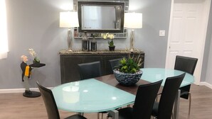 A dining area with a glass table, black chairs, a black cabinet, a TV above the cabinet, and two lamps on either side.