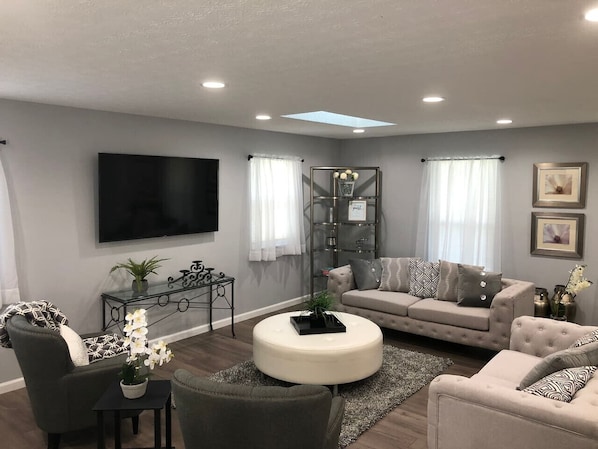A living room with a sofa, armchairs, a coffee table, a TV, and a glass cabinet.