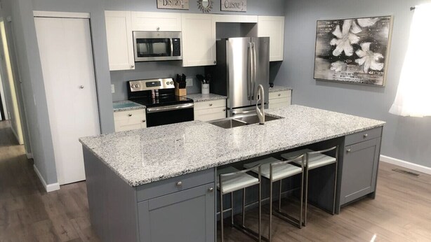 A kitchen with a granite countertop, stainless steel appliances, and a bar stool area.
