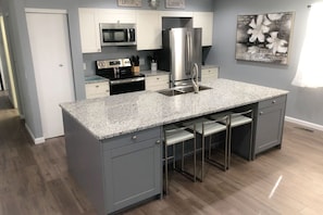 A kitchen with a granite countertop, stainless steel appliances, and a bar stool area.