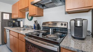 Una cocina con armarios de madera, una estufa de acero inoxidable, un microondas, una cafetera y un reloj en la pared.