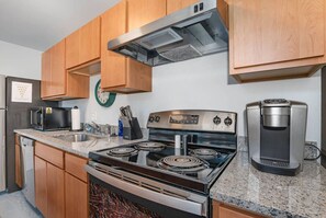 A kitchen with wooden cabinets, a stainless steel stove, a microwave, a coffee maker, and a clock on the wall. - 5103 Peters · New Industrial Loft on Lebanon Bike Trail !! (Maineville)