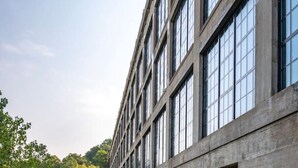 Un edificio con una extensa hilera de ventanas y un área cercada con mantillo.