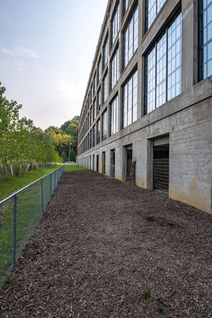 A building with a long side of windows and a fenced area with mulch. - 5103 Peters · New Industrial Loft on Lebanon Bike Trail !! (Maineville)