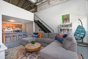 A modern living space with a grey sectional sofa, a round coffee table, a colorful rug, a bookshelf, and a hanging chair.