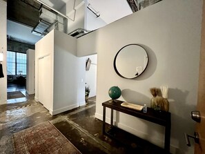 A hallway with a wooden floor, a round mirror on the wall, and a small table with a globe and decorative items.