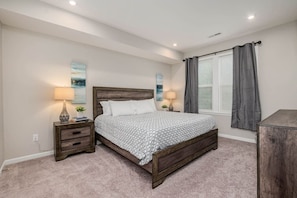 A bedroom with a wooden bed, two bedside tables with lamps, a window with curtains, and a painting on the wall.