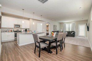 A modern kitchen with white cabinets, a central island, and a dining area with a dark table and chairs.
