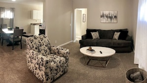 A living room with a sofa, a patterned armchair, a coffee table, and a dining area with a table and chairs. - 3311 Evanston · Large Renovated 4 BDR + Close to DTWN + Laundry (Cincinnati)