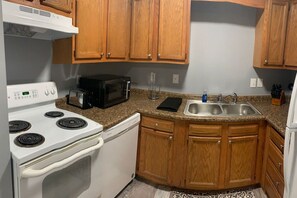 A kitchen with wooden cabinets, a white stove, a microwave, and a sink. - 5145 Porsche · Newly Remodeled 2 BDRM Ranch- Attached Home (Liberty Township)