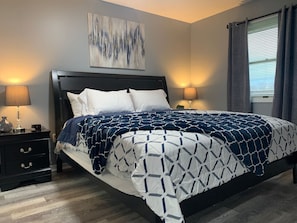 A bedroom with a bed, nightstands, a lamp, a painting, and a window with curtains. - 5145 Porsche · Newly Remodeled 2 BDRM Ranch- Attached Home (Liberty Township)