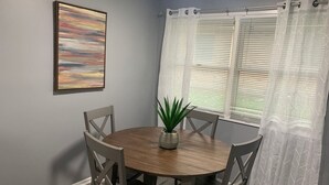 A dining area with a round table, four chairs, a potted plant, a framed picture, and a window with blinds. - 5145 Porsche · Newly Remodeled 2 BDRM Ranch- Attached Home (Liberty Township)