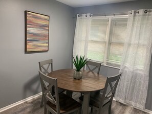 A dining area with a round table, four chairs, a potted plant, a framed picture, and a window with blinds. - 5145 Porsche · Newly Remodeled 2 BDRM Ranch- Attached Home (Liberty Township)