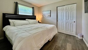 A bedroom with a bed, a nightstand, a window with curtains, a door, and a wall-mounted picture. - 219 Maxwell St - Unit A · Newly Renovated Franklin Flat (Franklin)