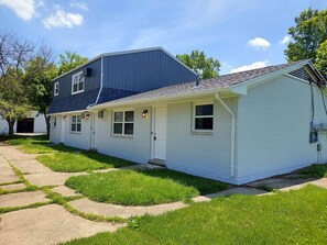 Ein zweistöckiges Haus mit Veranda, Auffahrt und Rasenfläche.