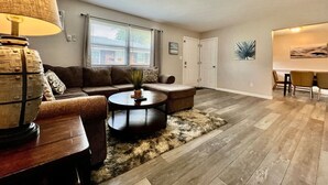 A living room with a sectional sofa, a round coffee table, and a lamp. There is a dining area with a table and chairs. - 219 Maxwell St - Unit A · Newly Renovated Franklin Flat (Franklin)