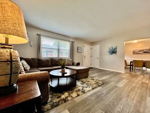Ein Wohnzimmer mit Sofa, Couchtisch und Lampe. Es gibt eine Essecke mit Stühlen und einem Tisch.