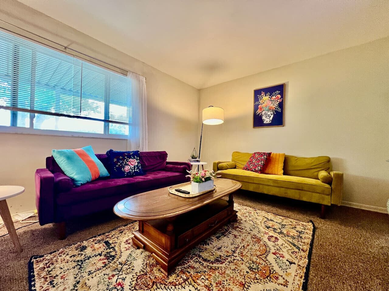 A living room with a purple sofa, a yellow sofa, a wooden coffee table, and a patterned rug.