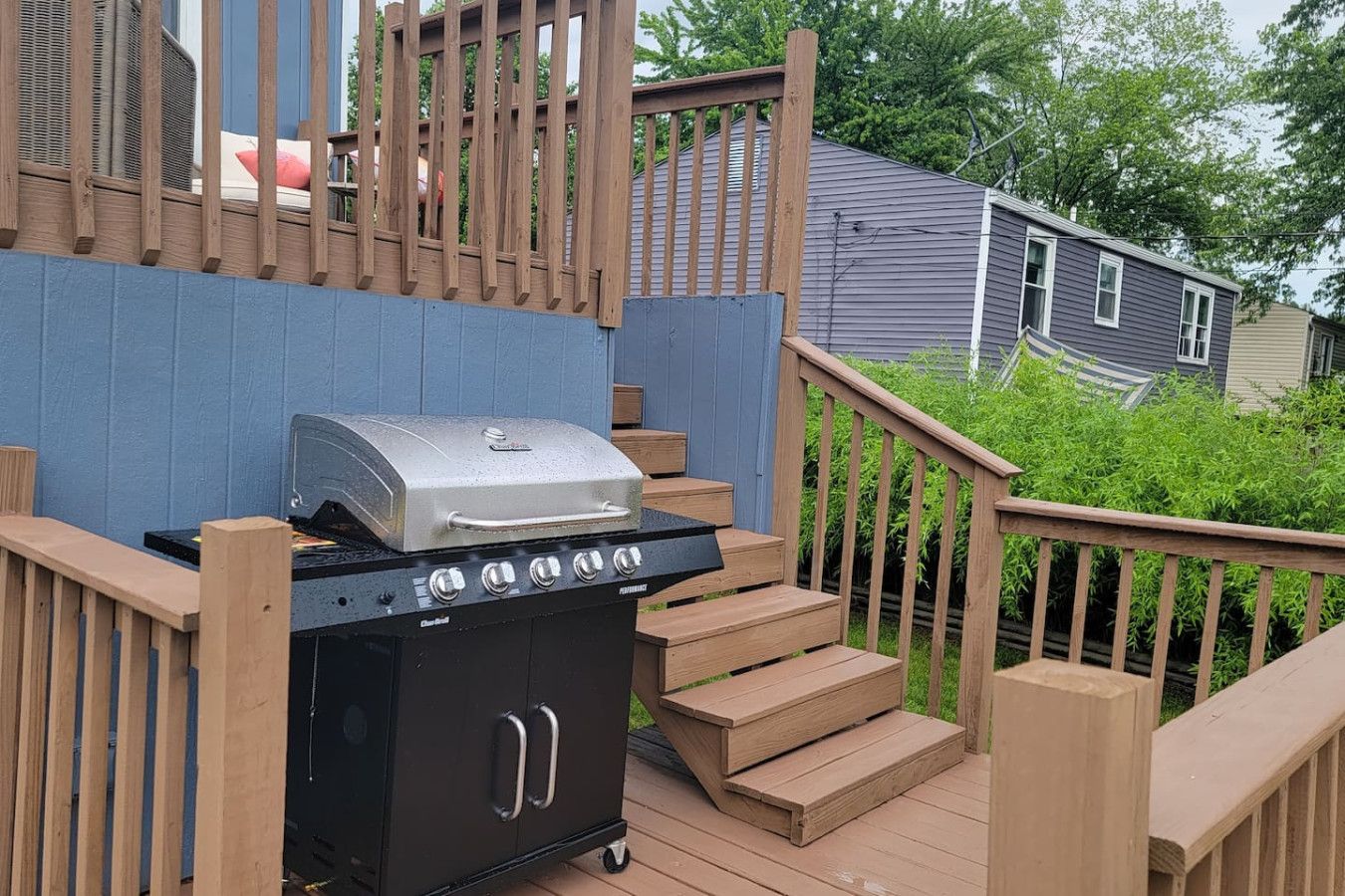 Un barbecue sur une terrasse en bois, avec un mur bleu et un escalier.